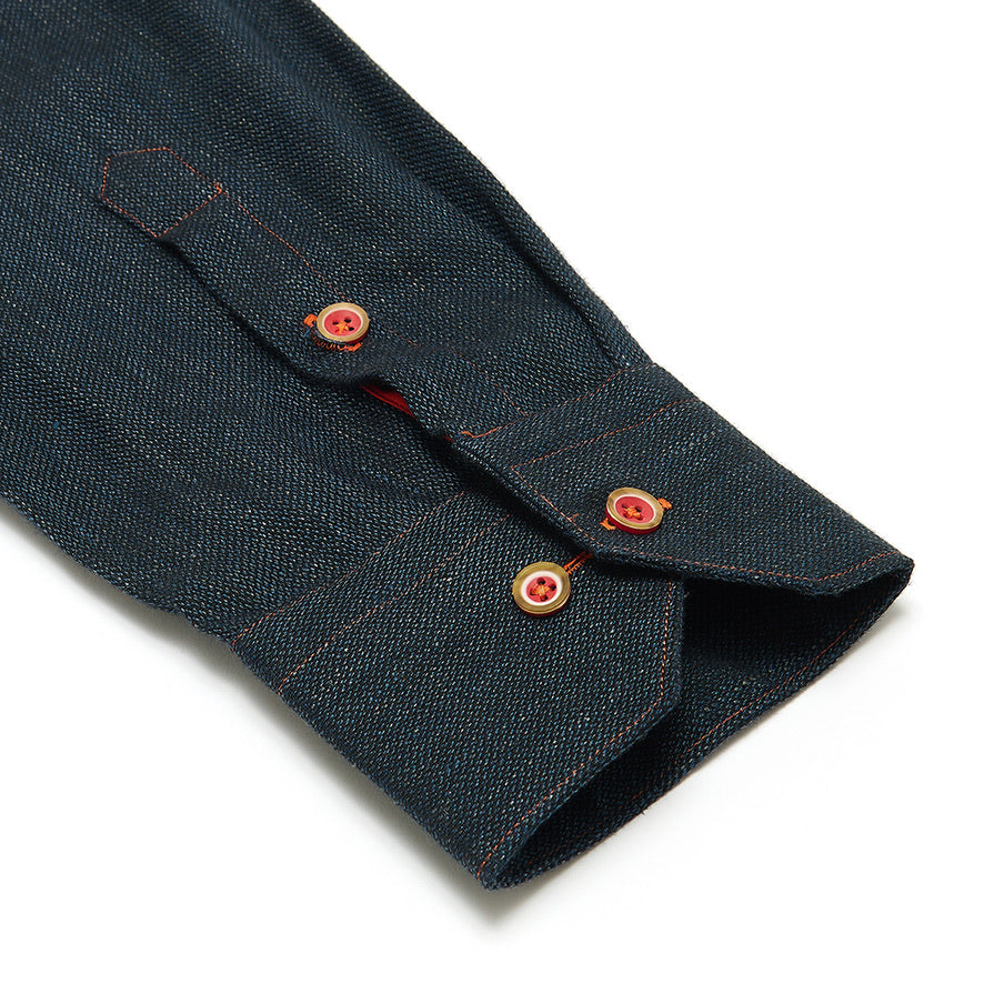 Close-up of a dark denim shirt sleeve with red buttons on a white background
