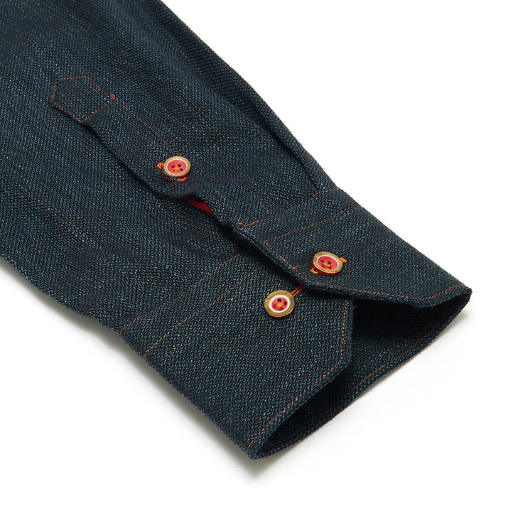 Close-up of a dark denim shirt sleeve with red buttons on a white background